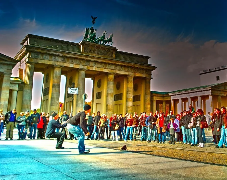 Das Brandenburger Tor mit Strassenkünstler und Touristengruppe davor unter dramatischem Himmel.