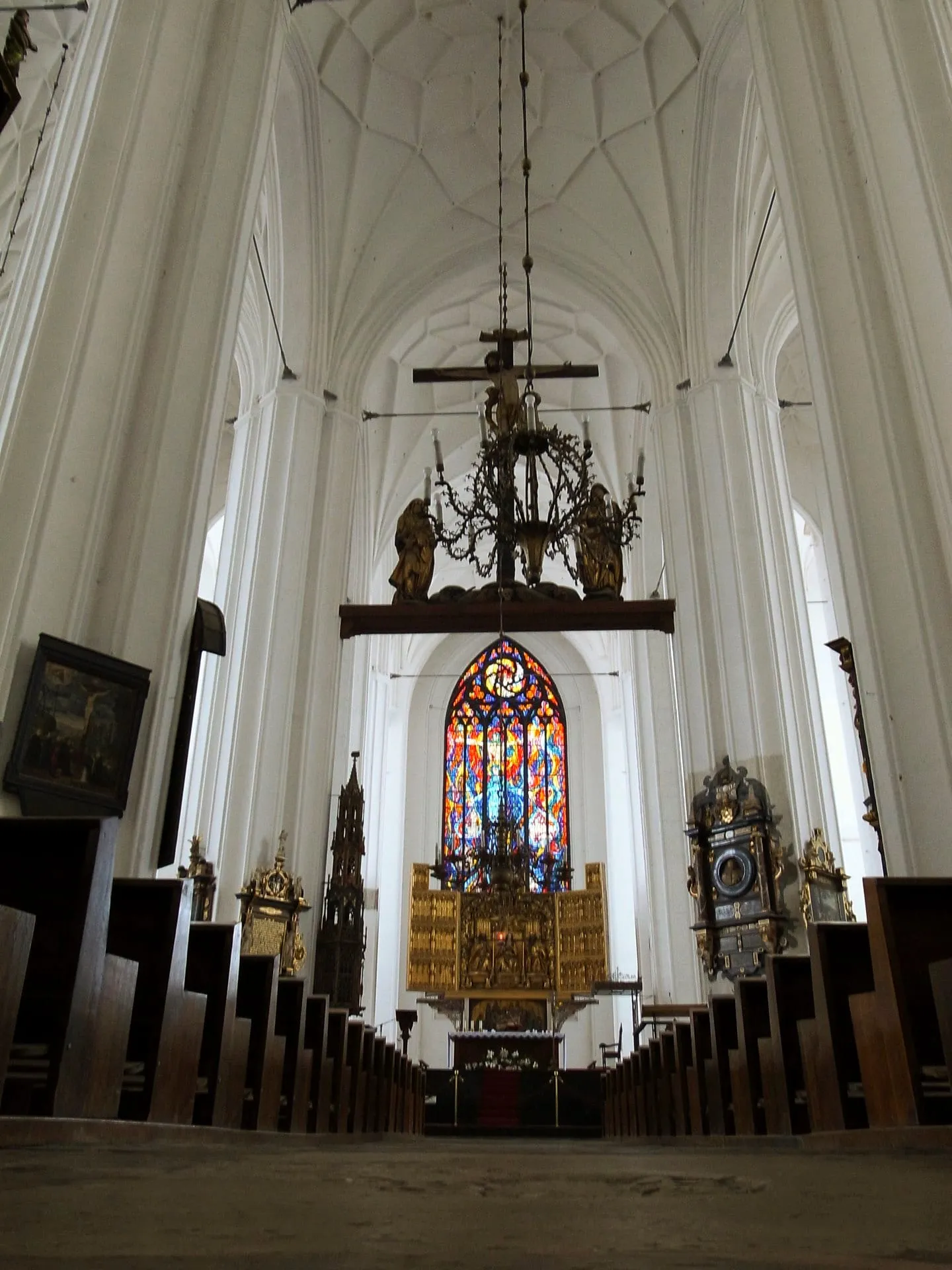 Weisses Kirchenschiff mit Buntglasfenster und barockem Altar.