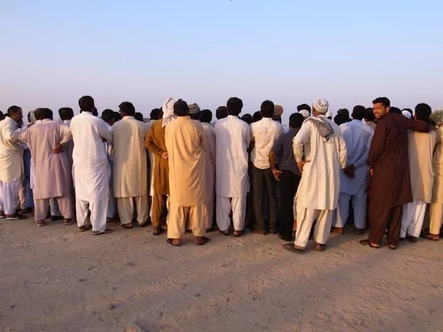 Eine grosse Gruppe Männer in traditioneller Kleidung steht dicht gedrängt in der Wüste.