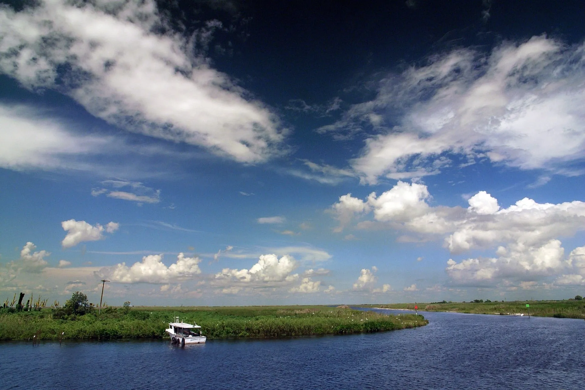 Ein Ausflugsboot fährt durch einen Wasserkanal der Everglades unter weiten Wolken.