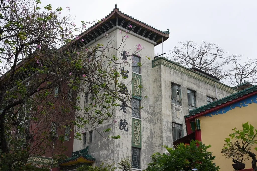 Historisches Gebäude im chinesischen Kolonialstil mit geschwungenem Dach zwischen Bäumen.